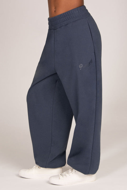 A person wearing wide-leg navy sweatpants with an elastic waistband and white sneakers, shown from the waist down against a light grey studio background.