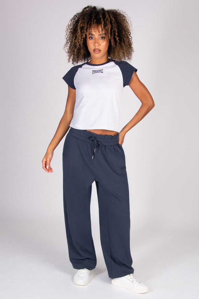Woman wearing a white and navy baseball t-shirt with matching oversized joggers on a white background