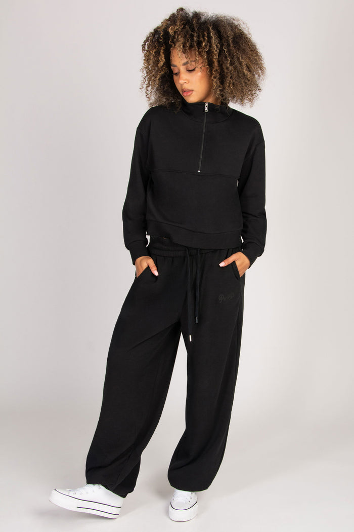 Model wearing super baggy black joggers with functional pockets, paired with a zip-front sweatshirt.