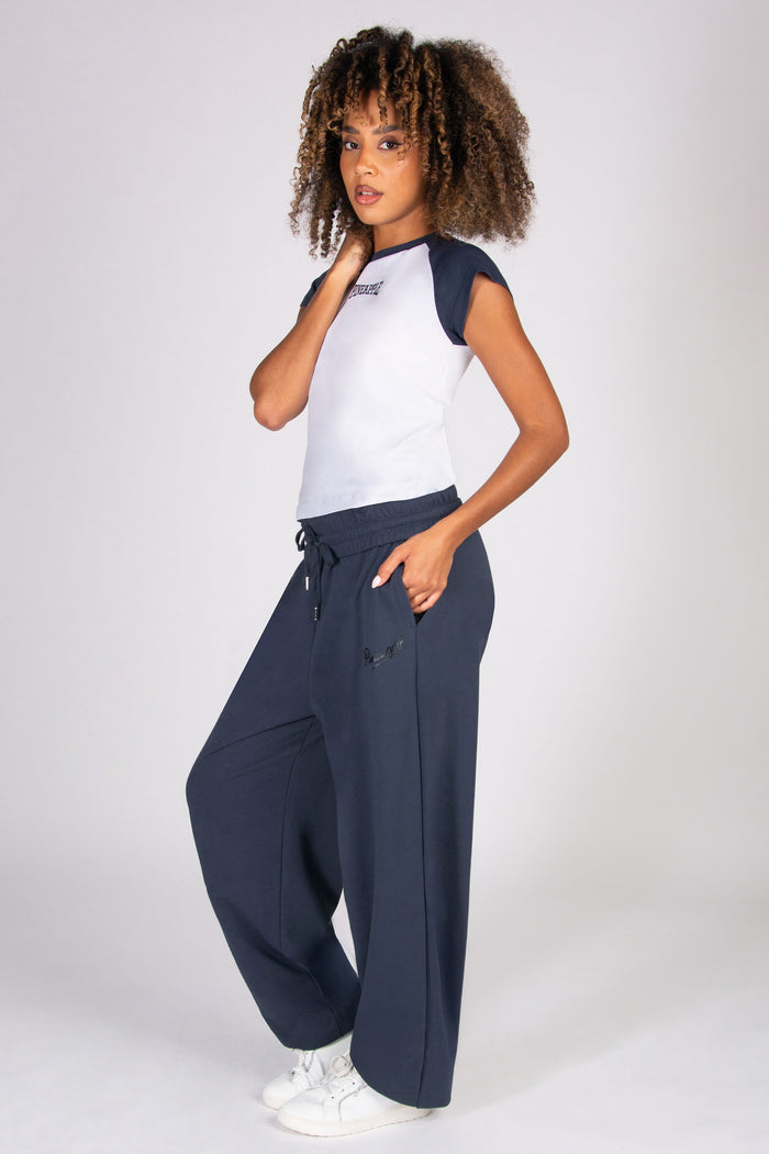 Woman wearing a white and navy t-shirt with low-waisted baggy navy pants on a white background
