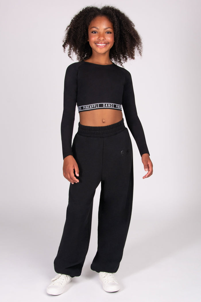Girl wearing a black long-sleeve crop top and black oversized joggers on a white background