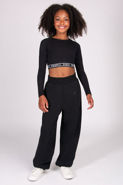 Girl wearing a black long-sleeve crop top and black oversized joggers on a white background