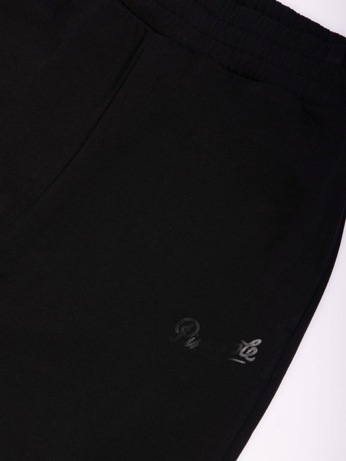 Close-up of oversized black joggers with tonal printed logo and side pockets.