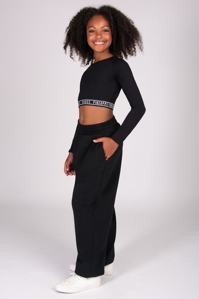 Girl wearing a black long-sleeve top and wide-leg joggers on a white background
