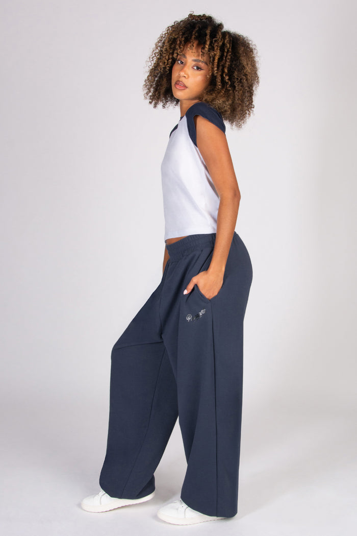 Woman wearing a white top and navy wide-leg joggers on a white background