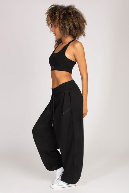 Streetwear look featuring woman in extra loose black joggers and mesh crop sports bra.