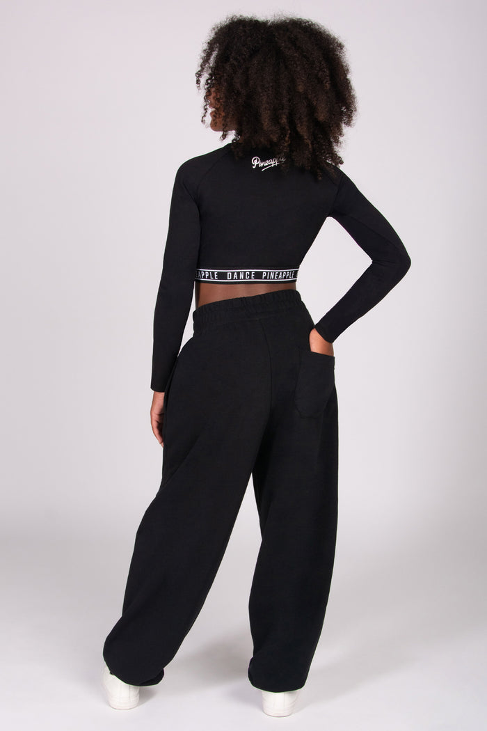 Person wearing a black long-sleeve crop top and black joggers with back pocket on a white background