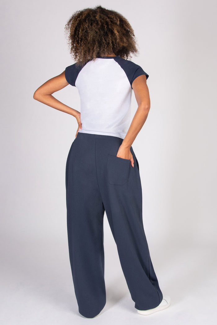 Woman wearing a dark grey baggy joggers on a plain background