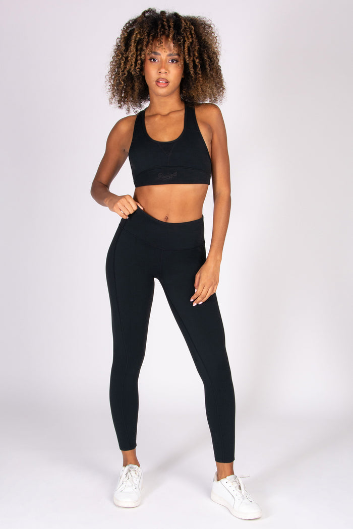 Woman wearing black super soft 7/8 yoga leggings with matching sports bra on a white background