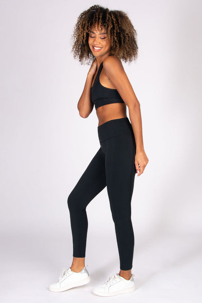 Woman wearing black super soft 7/8 yoga leggings with matching sports bra on a white background