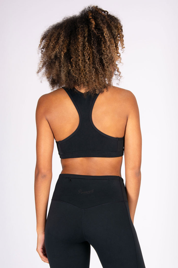 Woman wearing a black sports bra and leggings with hidden zip pocket on a white background