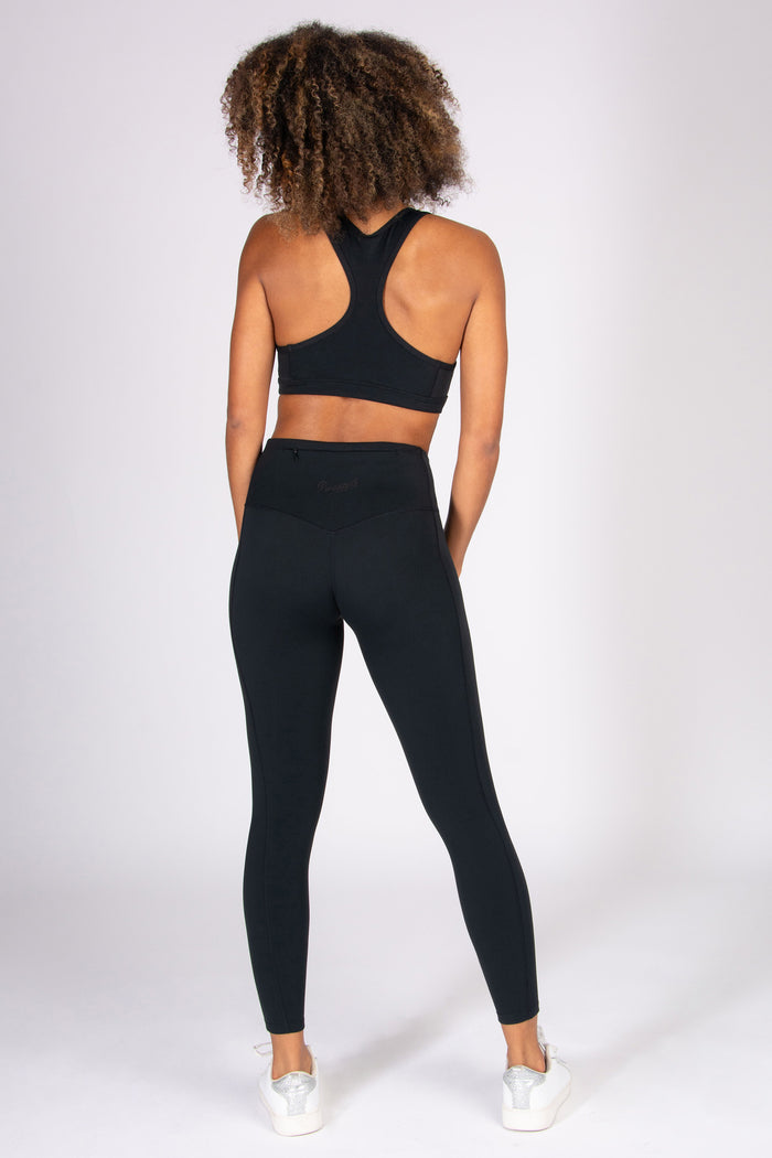 Woman wearing black super soft 7/8 yoga leggings with matching sports bra on a white background