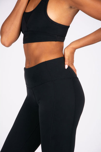 Person wearing black athletic leggings and sports bra on a white background