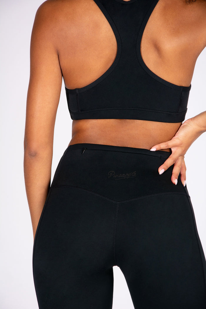 Woman wearing a black super soft sports bra and matching cycling shorts with hidden zip pocket on a white background