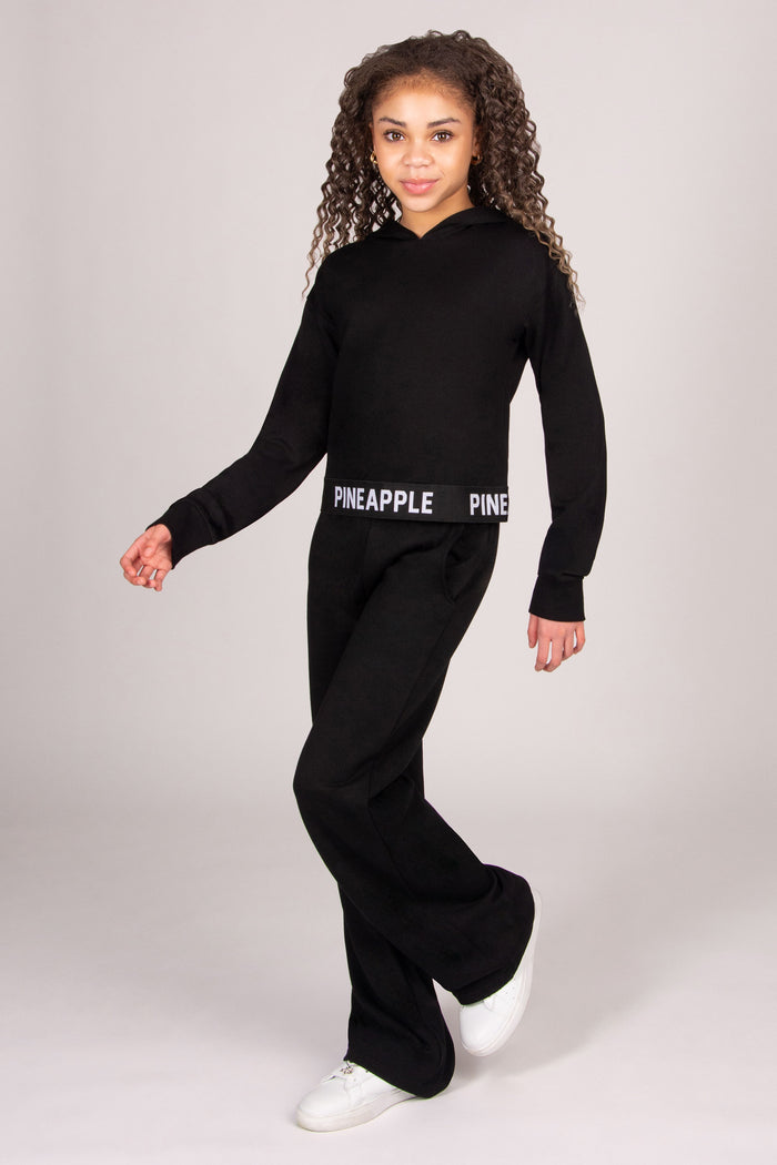 Girl wearing a black dance hoodie with matching wide leg trousers against a light grey background.