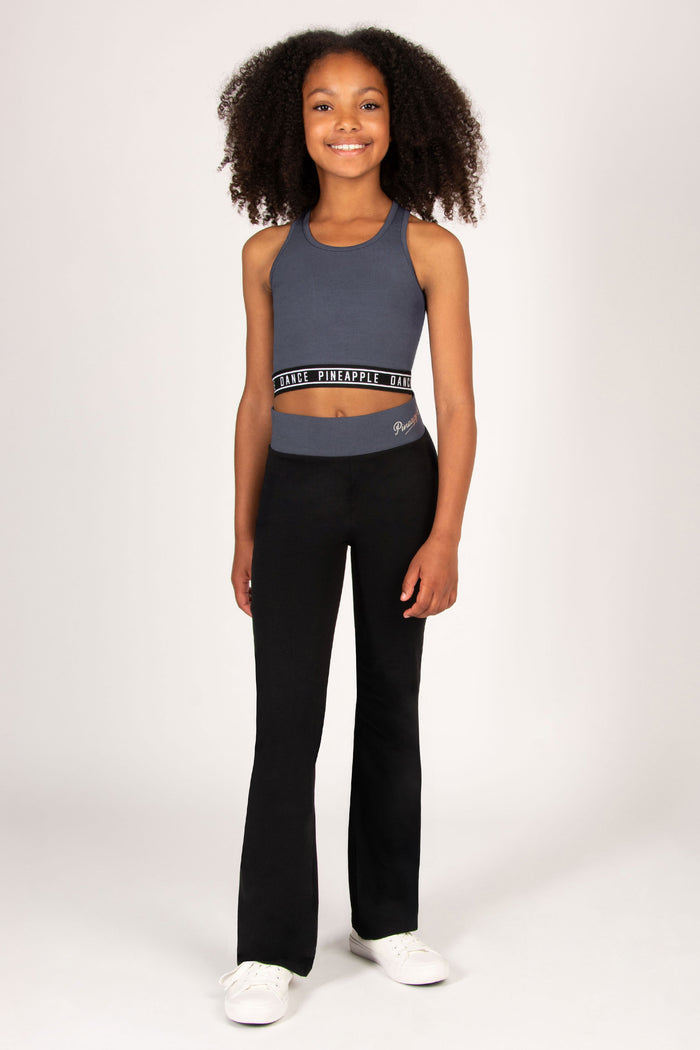 Teen wearing a charcoal crop top and matching black flared pants on a white background