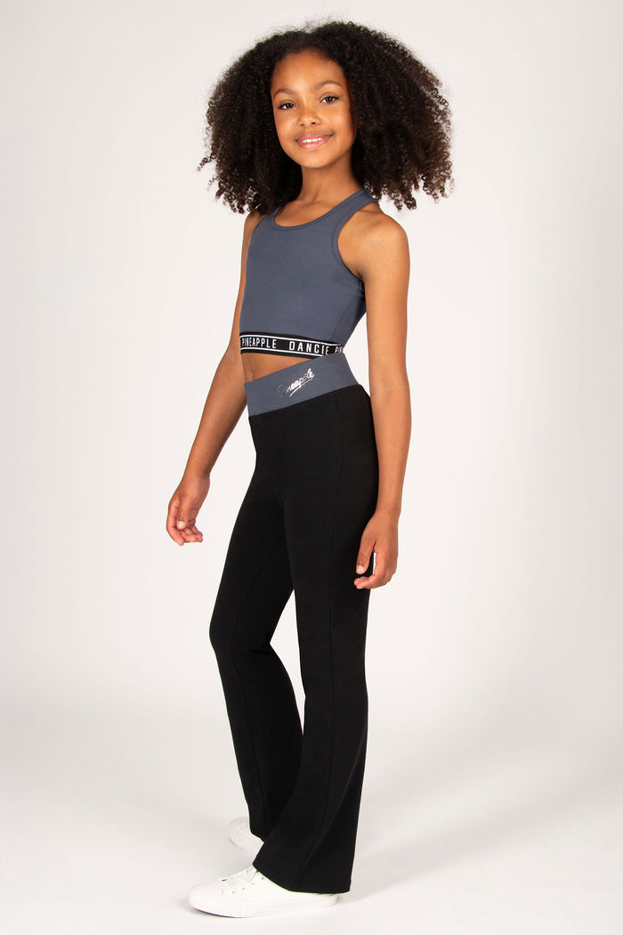Young girl wearing a charcoal sports crop top and black pants on a white background