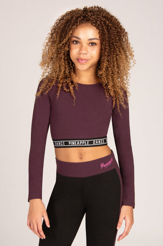 Girl wearing a maroon brown long-sleeve crop top and matching black flared trousers on a plain background