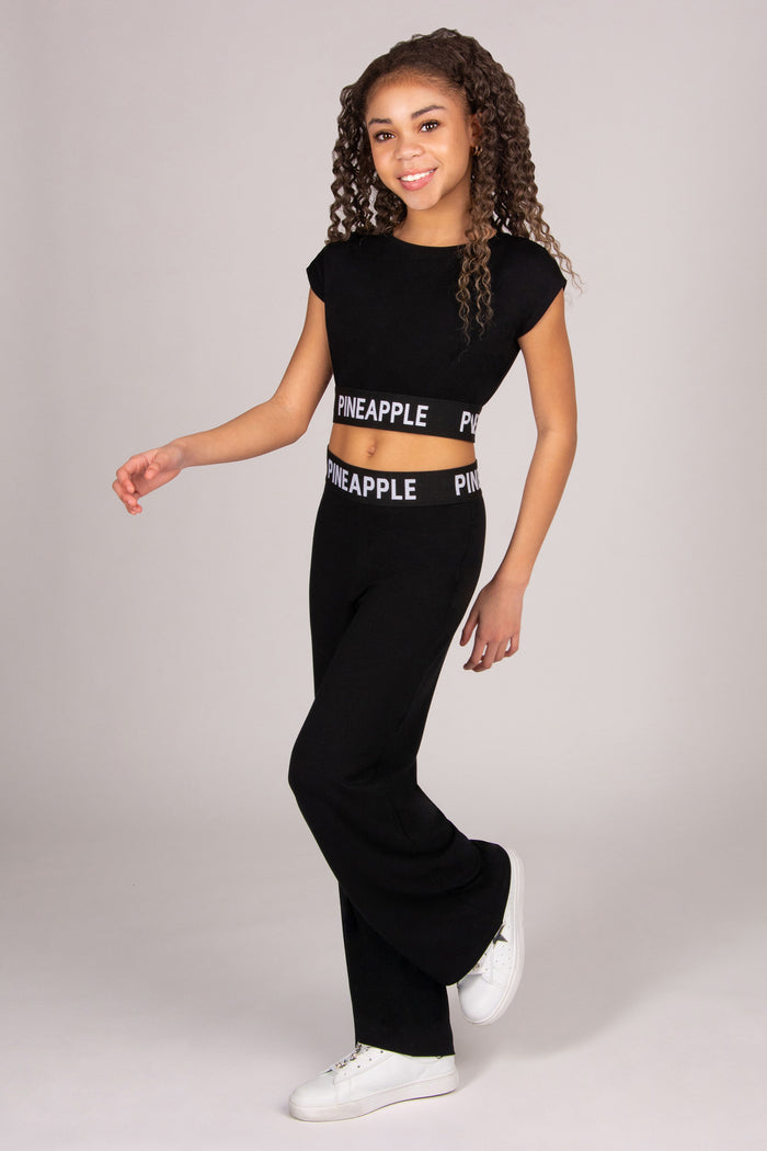 Girl wearing a black dance crop top and wide leg trousers on a plain background