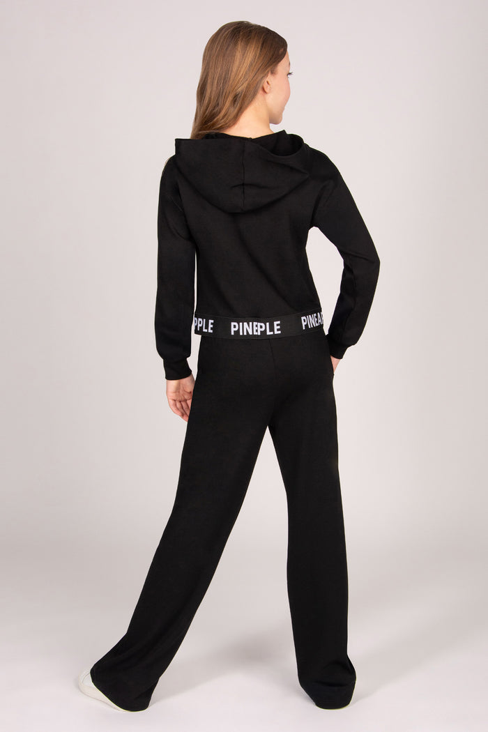 Girl wearing a black wide leg joggers against a plain background.
