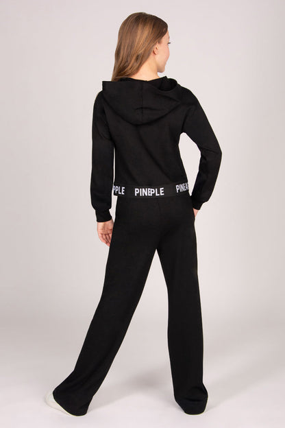 Girl wearing a black wide leg joggers against a plain background.
