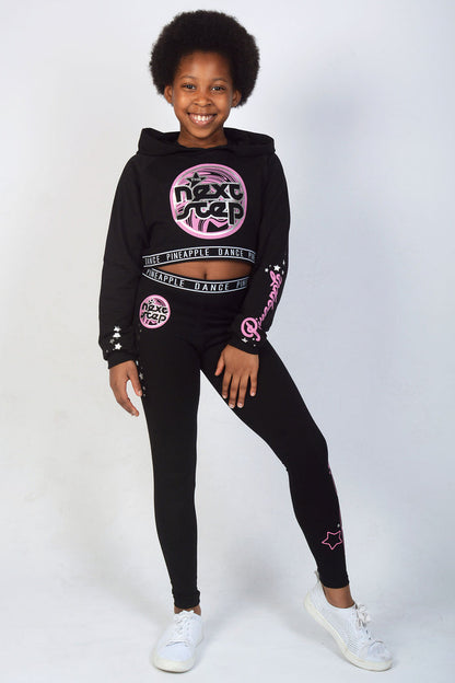 Girl wearing Black The Next Step Crop Hoodie with pink logos and matching jacquard leggings