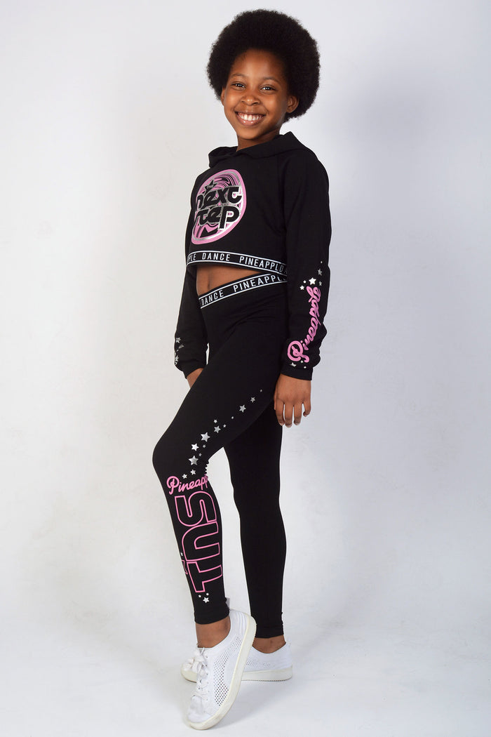 Girl wearing Black The Next Step Crop Hoodie and matching jacquard leggings with pink logos