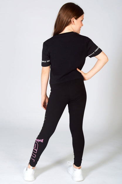 Girl wearing matching The Next Step dance wear featuring Pineapple crop black t-shirt and TNS leggings with silver star details.