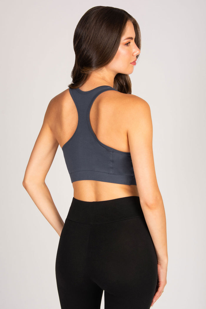 Woman wearing a dark grey sports bra and black leggings on a light background