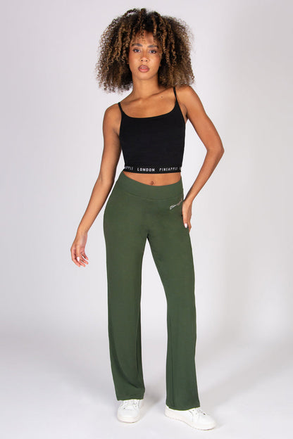Woman wearing a black tank top and khaki wide leg yoga pants on a white background