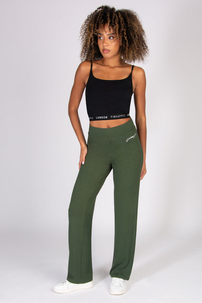 Woman wearing a black tank top and khaki wide leg yoga trousers on a white background