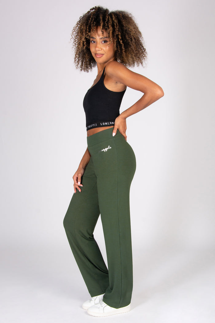 Woman wearing a black tank top and khaki wide leg yoga trousers on a white background