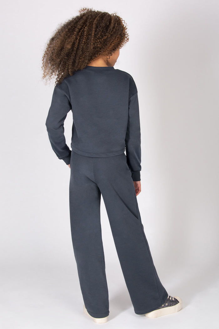 Girl wearing a dark grey matching sweatshirt and wide leg trousers on a white background