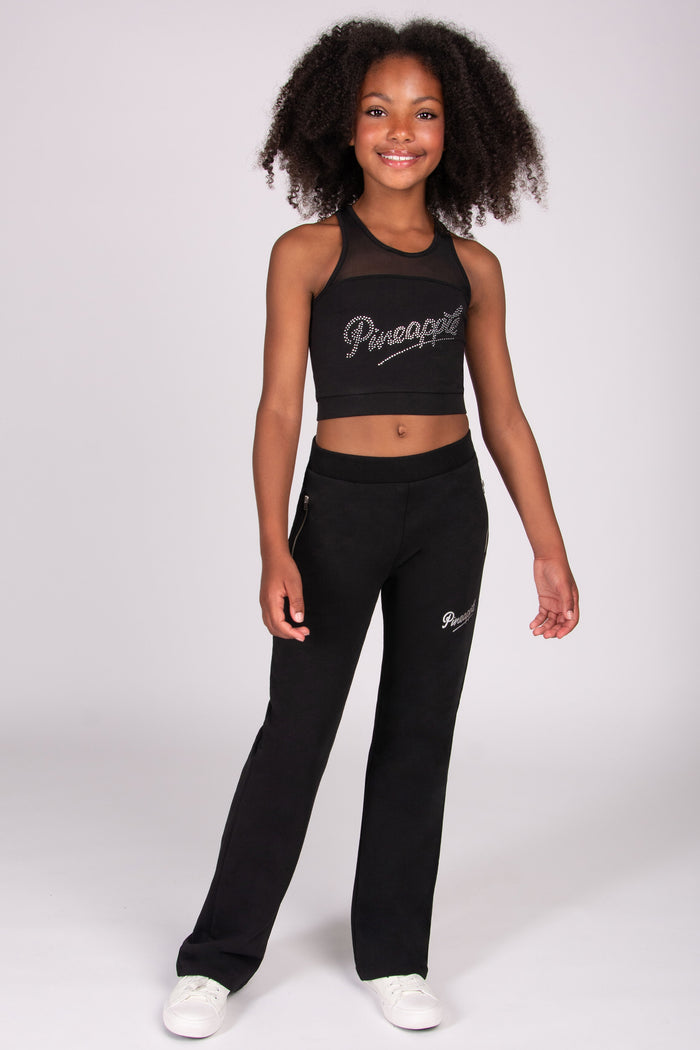 Young girl wearing a black flared trousers with 'Pineapple' branding on a white background