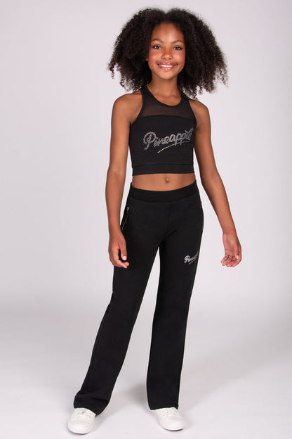 Young girl wearing a black flared trousers with 'Pineapple' branding on a white background